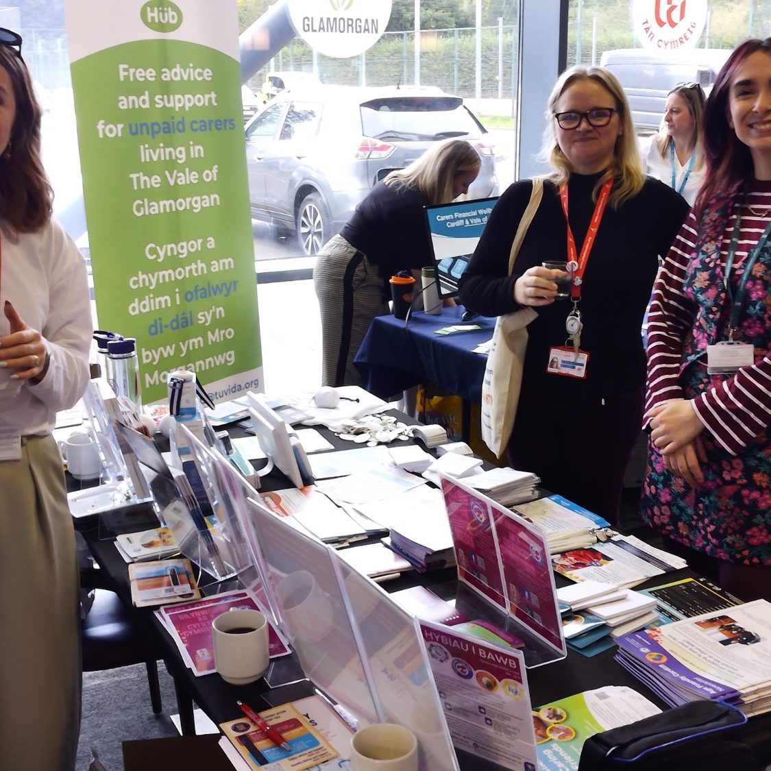 Two women stand at a display table with promotional materials, engaging with visitors.