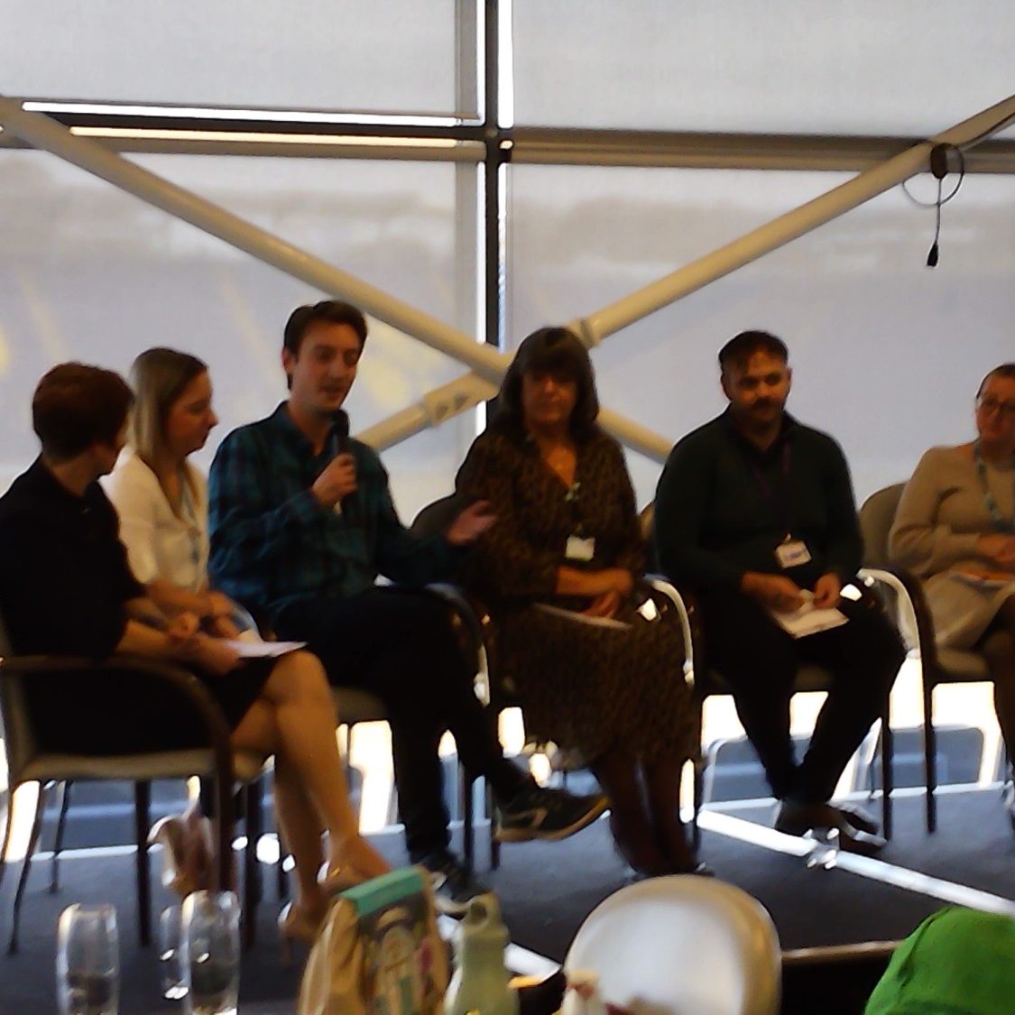 A panel discussion featuring five speakers seated in a modern conference setting.